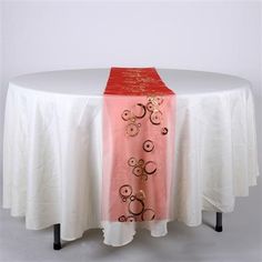 a white table with a pink and gold runner on it's side, sitting next to a white round tablecloth