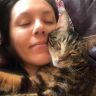 a woman laying on top of a couch next to a brown and white cat with her eyes closed