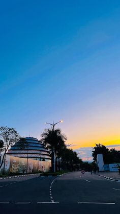 an empty street at dusk with palm trees in the foreground and a building on the far side