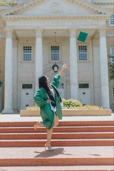 a woman in a green graduation gown is throwing her cap into the air while standing on some steps