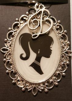 a brooch with a silhouette of a woman's head in the center and an initial at the bottom