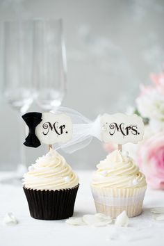 two cupcakes with white frosting and black bows are on the table next to each other