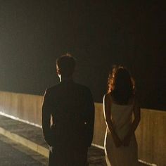 a man and woman standing next to each other on the side of a road at night