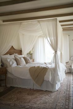 a bed with white drapes and pillows in a bedroom next to a large window