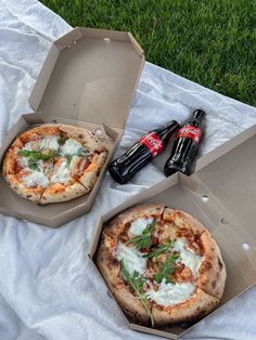 two pizzas sitting on top of a white blanket next to bottles of beer and soda