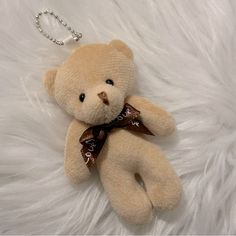 a teddy bear with a brown ribbon on it's neck laying on a white fur surface