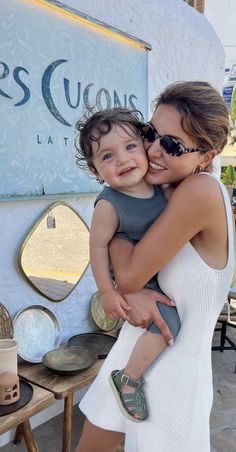 a woman holding a child in front of a sign that says kris cussons