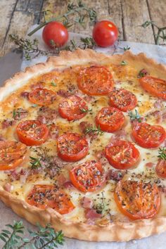 an uncooked pizza with tomatoes and herbs on the table next to two tomatoes