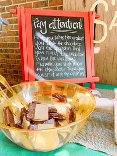 a bowl filled with chocolate and marshmallows next to a chalkboard sign