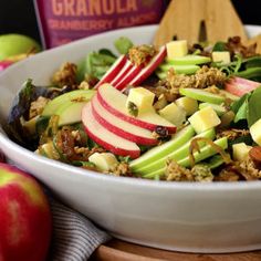 an apple and walnut salad in a white bowl with wooden utensils next to it