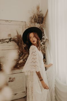 a woman in a white dress and black hat standing next to a bed with feathers on it