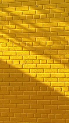 a yellow brick wall with the shadow of a tree casting a long shadow on it