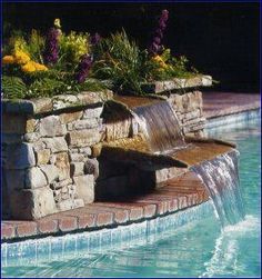 a water feature in the middle of a swimming pool with flowers growing on either side