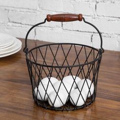 four white balls in a wire basket on a wooden table next to plates and a brick wall