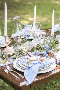 a table set with plates and candles for an outdoor dinner party in the grass outside