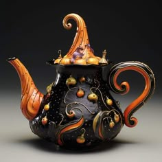 a black teapot with orange and gold designs on it