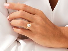 a woman's hand wearing a gold ring with a square shaped diamond on it