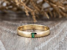 a yellow gold wedding band with a green stone in the center on a wooden surface