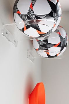 three soccer balls hanging from the ceiling in a room with white walls and orange accents