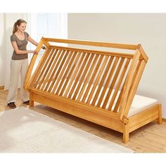 a woman standing next to a wooden bed frame with mattress on it's side