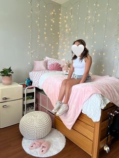 a woman sitting on top of a bed next to a white heart shaped pillow and stuffed animal