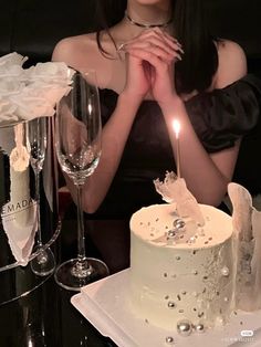 a woman sitting in front of a white cake with a candle on top of it