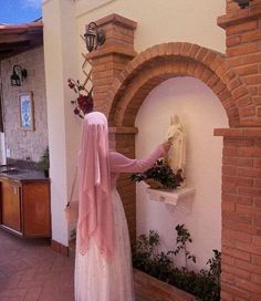 a woman in a veil is placing flowers on a statue near a brick wall and archway