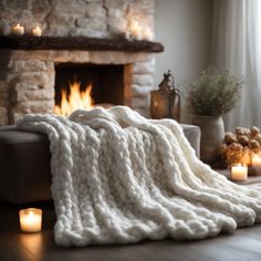 a white blanket sitting on top of a wooden floor next to a fireplace covered in candles