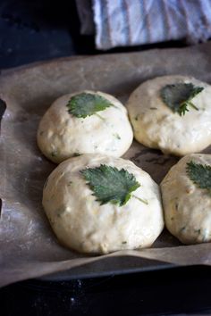 four round breads with green leaves on them sitting on wax paper in a baking pan