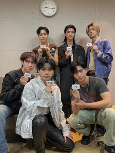 group of young men holding up small cards in front of a wall with a clock