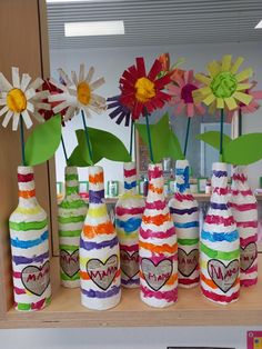 colorful vases with flowers in them sitting on a shelf next to other bottles and papers