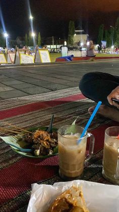 a man sitting at an outdoor table with food and drinks in front of him on his cell phone