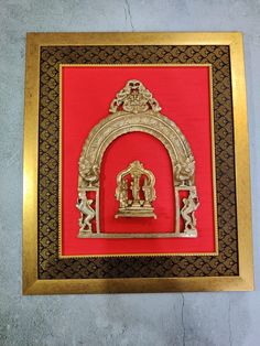 an ornate gold and red frame with a clock on it's side in front of a wall