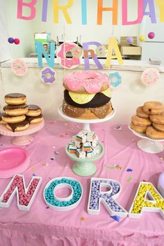 a pink table topped with lots of doughnuts and other desserts next to a happy birthday sign