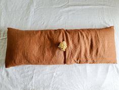 a brown pillow with a flower on it sitting on a white bed sheet covered in linen