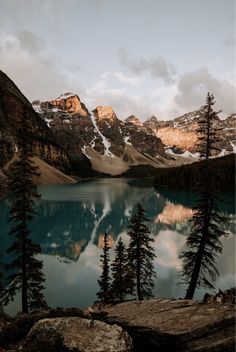 a lake surrounded by mountains and trees with snow on the tops in the evening light