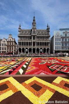 an elaborately designed carpet in the middle of a square with buildings and people walking around it