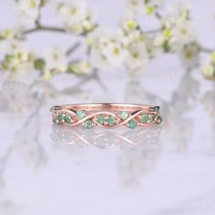 a rose gold ring with green stones on it and some flowers in the back ground