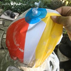 a person holding up a plastic bag filled with different colored items on top of a stone wall