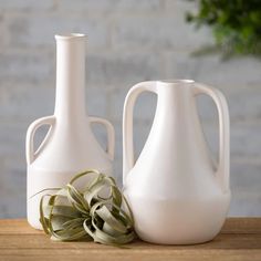 two white vases sitting on top of a wooden table