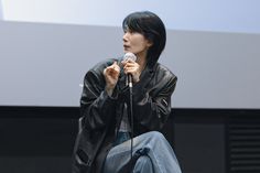 a woman holding a microphone in her right hand and sitting on the floor next to a projector screen