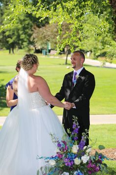 a bride and groom holding hands under a tree at their wedding ceremony in the park