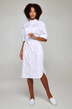 This fashionable  lab coat will make any female doctor or a beautician look stylish and classy when at work.  The elegant uniform dress has a comfortably fitted silhouette of a midi length. It has mockneck and side cuts and fastens with hidden buttons.  The width of the sleeves can be adjusted with the help of buttoned plackets.  The dress is completed with 2 belts that allow changing the dress's look and make the silhouette more elegant and slender.  The fabric is 70% cotton, 30% polyester, mad Nurse Scrub Dress, Beautician Uniform, Lab Coat Fashion, White Nurse Dress, Doctor Clothes, Nurse Style, Medical Scrubs Fashion, Scrub Uniform, Nurse Dress Uniform