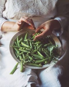 a woman is holding a plate full of green beans and pea pod sprouts