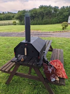 an outdoor bbq grill sitting on top of a picnic table next to a red bag