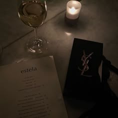 a table topped with a glass of wine and a menu next to a lit candle