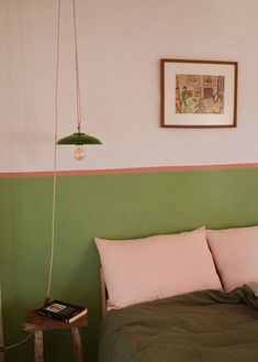 a bed with green sheets and pink pillows in a bedroom next to a painting on the wall