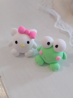 two hello kitty dolls sitting next to each other on a white tablecloth covered surface