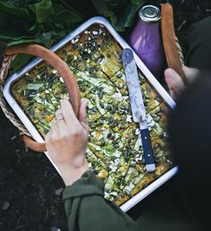 a person holding a tray with food on top of it next to vegetables and a knife