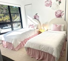 two beds with pink and white bedding in a bedroom next to a large window